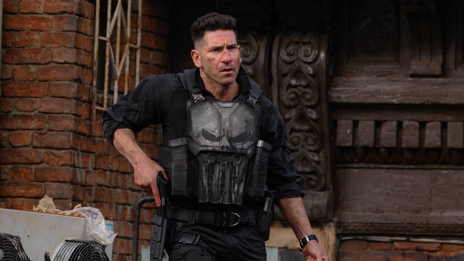 Rollfiguren The Punisher i svart skyddsväst med dödskalle framför en tegelvägg
