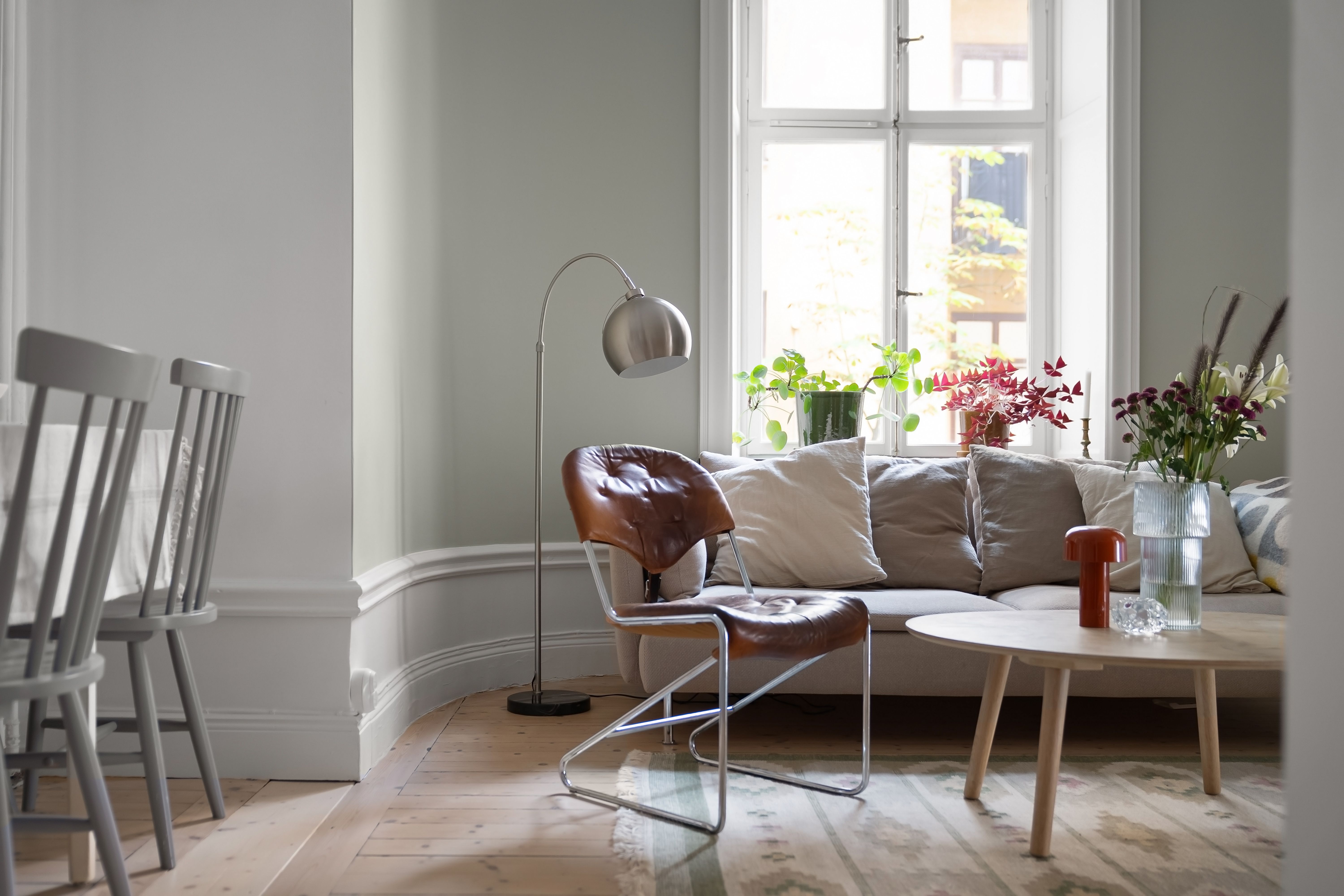 Vardagsrum med läderfåtölj i krom, båglampa, grå soffa och runt soffbord