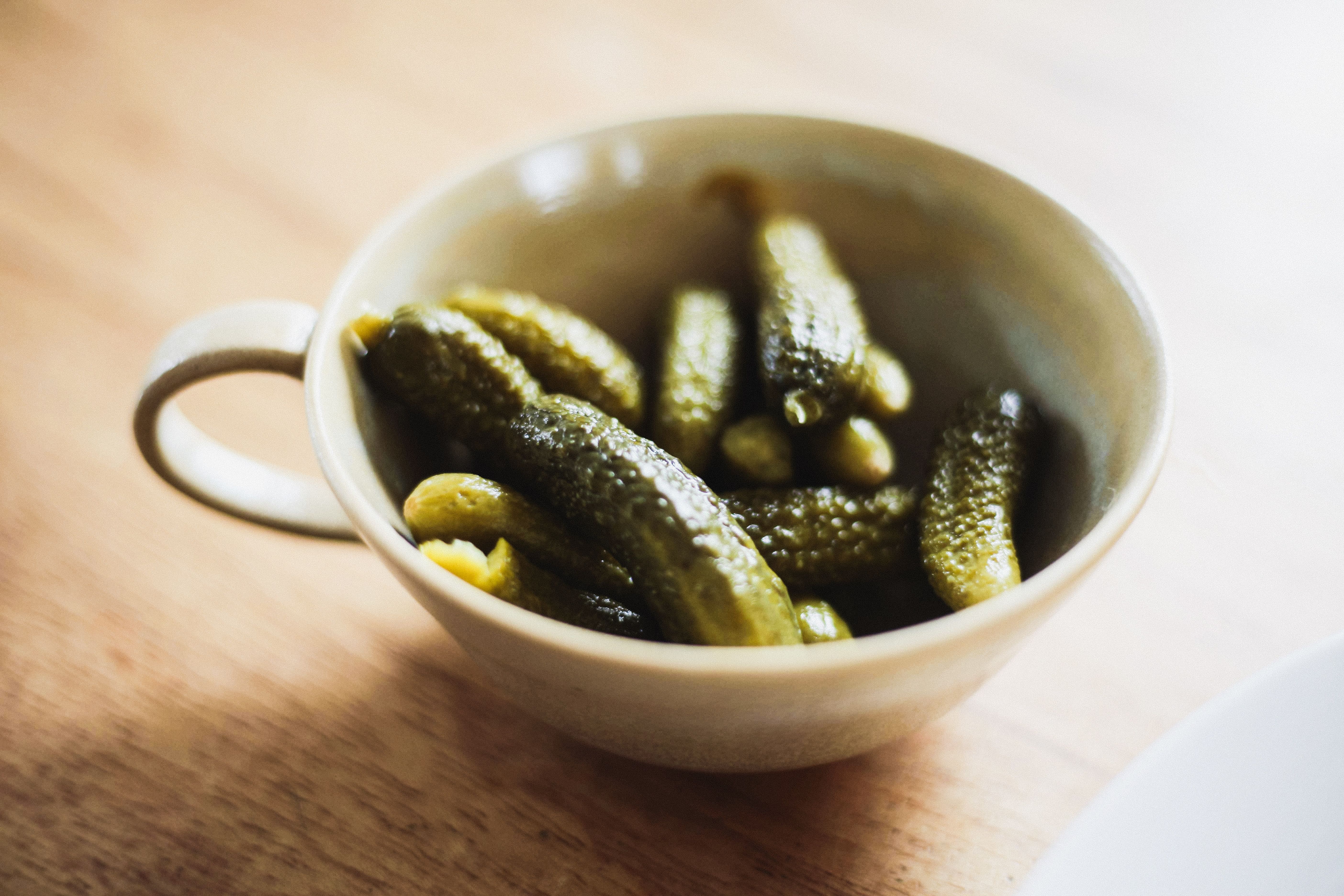 Cornichons i en liten keramikkopp på ett träbord