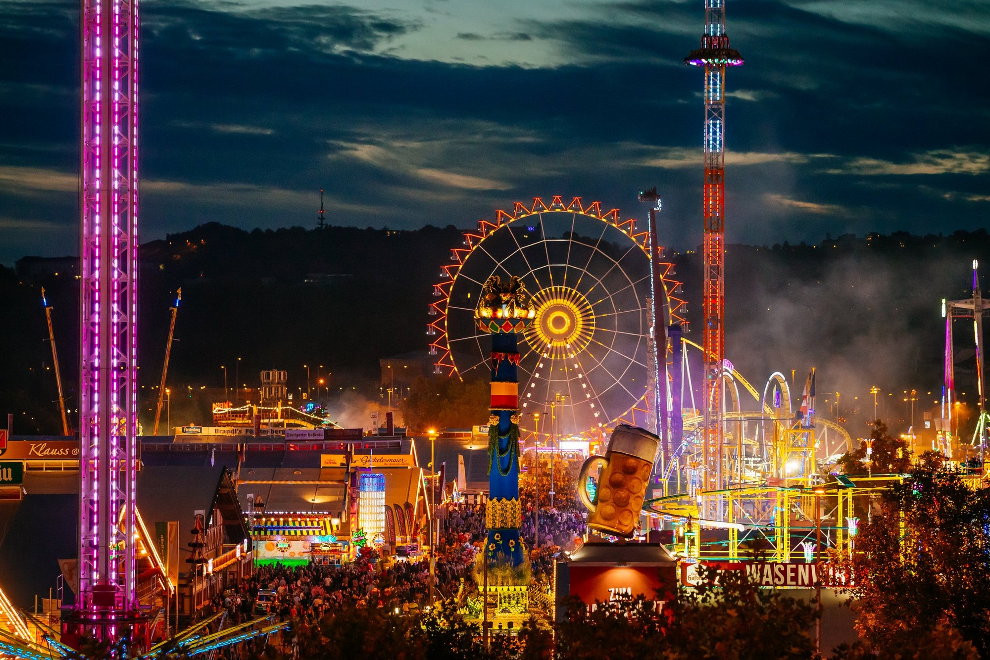 Cannstatter Volksfest i kvällsljus med upplyst pariserhjul, karuseller och ölsejdel